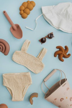Şık İskandinav İskandinav bebek plaj oyuncakları ve pastel mavi arka planda giysiler. Plajda oynamak için bebek eşyaları. Düz yatış, üst görünüm