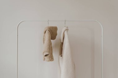 Ilık sonbahar bebeği ve beyaz duvarda asılı yetişkin kıyafetleri. Yünlü nötr bej, beyaz ve siyah ceketler. Minimalist moda kıyafet dolabı.