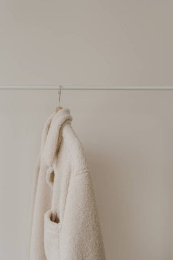 Beyaz duvarda asılı duran beyaz, sıcak, yünlü sonbahar sezonu ceketi. Minimalist moda kıyafet dolabı.