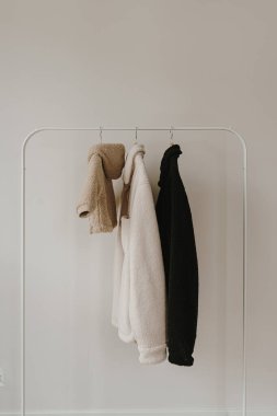 Sonbahar kıyafetleri beyaz duvardan sarkıyor. Sıcak bebek ve yetişkin ceketleri. Kıyafetleri tarafsız renklerde olan estetik bir gardırop.