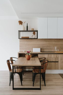 Modern İskandinav ev iç tasarımı. Parlak açık oturma odası, yemek masası, mutfak mobilyası, sandalyeler, dekorasyonlar. Kira konsepti için şık bir daire.