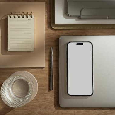 Boş ekranlı cep telefonu, dizüstü bilgisayarı, tableti, defteri, bir bardak suyu olan düz konutlu ofis çalışma alanı. Sabah işi, iş konsepti. Masada güneş ışığı gölgeleri var. Düz konum, üst görünüm, kopyalama alanı