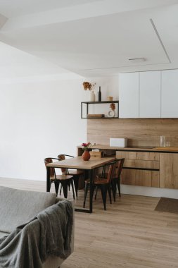 Modern yeni apartman iç tasarımı. Mutfak eşyaları, raflar, yemek masası, sandalyeler olan beyaz mobilyalar. Kiralık daireler