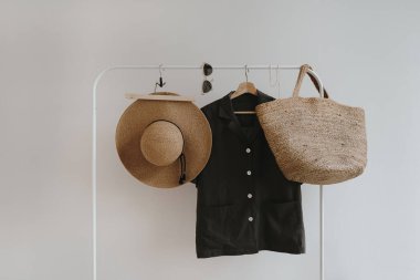 Estetik kadın kıyafetleri. Şık kadın bluzu, hasır şapka, saman el çantası, askıda güneş gözlüğü. Minimalist moda günlüğü