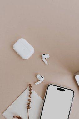 Boş ekranlı cep telefonu, kablosuz kulaklıklar, bej masadaki kurutulmuş çimenler. Sosyal medya için estetik nötr şablon, model için kopyalama alanı olan mobil web sitesi