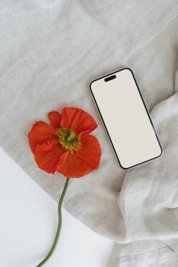 Model kopyalama alanı ve buruşuk kumaş üzerinde haşhaş çiçeği olan boş bir ekran cep telefonu. Minimum estetik marka şablonu. Düz yatış, üst görünüm