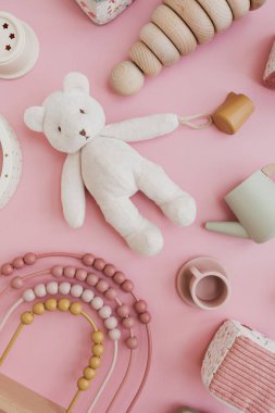 Pembe arka planda bebek eşyalarının olduğu düz bir set. İskandinav doğal tahta bebek oyuncakları