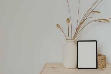 Tablet, nötr bej kil çömlek, kurutulmuş çimenler ve gelincikler, ahşap masa üzerinde ahşap tabut beyaz duvarın üzerinde. Boş boş kopya alanı boş ped ekran ile estetik maket