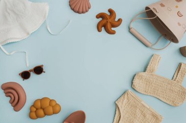 Küçük bebek organik plaj oyuncakları, moda kıyafetleri ve pastel mavi arka planda aksesuarlar. Düz yatar, üst görünüm boş kopya alanı oluşturur
