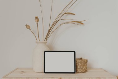 Tablet, nötr bej kil çömlek, kurutulmuş çimenler ve gelincikler, ahşap masa üzerinde ahşap tabut beyaz duvarın üzerinde. Boş boş kopya alanı boş ped ekran ile estetik maket