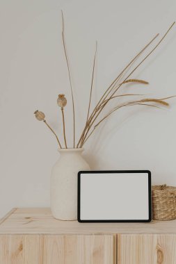 Tablet, nötr bej kil çömlek, kurutulmuş çimenler ve gelincikler, ahşap masa üzerinde ahşap tabut beyaz duvarın üzerinde. Boş boş kopya alanı boş ped ekran ile estetik maket