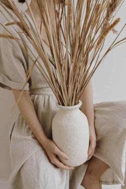 Çamur tenceresi ve kurutulmuş otlar kadınların elinde. Tarafsız ten rengi keten elbise giyen genç ve güzel bir kadın..