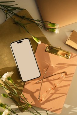 Beyaz perdeli akıllı telefon ve karanfil çiçekleri. Estetik güneş ışığı gölgeleri. Ofis masası çalışma alanı. Model kopyalama alanı ile en küçük iş markalaştırma şablonu