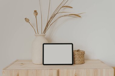 Boş ekranlı tablet tableti, kuru otlu kil tabut ve beyaz duvarda haşhaş sapı. Sosyal medya için estetik nötr bej şablonu, model için kopyalama alanı olan mobil web sitesi