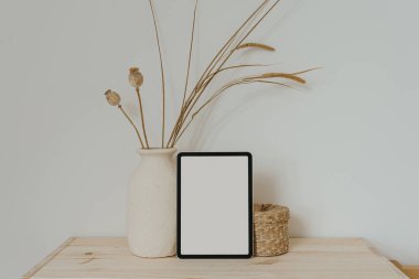Boş ekranlı tablet tableti, kuru otlu kil tabut ve beyaz duvarda haşhaş sapı. Sosyal medya için estetik nötr bej şablonu, model için kopyalama alanı olan mobil web sitesi