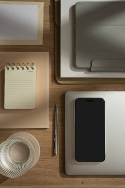 Cep telefonu, dizüstü bilgisayar, tablet tablet, defterler, kağıt çarşaflar, ahşap masadaki bir bardak su. Estetik ofis çalışma alanı. Günlük, sosyal medya, web, dergi şablonu