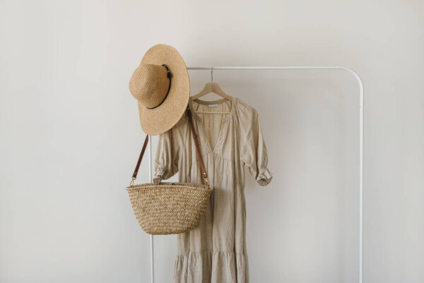 Elegant fashion clothes and accessories. Beige linen dress, straw hat, straw handbag on hanger. Fashion blog, social media template with copy space
