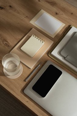 Ofis masası çalışma alanı telefon, dizüstü bilgisayar, spiral çevirmeli defter, tablet, masa üzerinde güneş ışığı gölgeli bir bardak su. Günlük, web sitesi, sosyal medya hesabı markalaşması