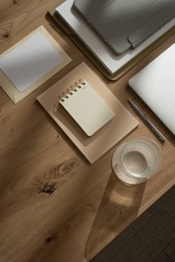 Evde çalış. Laptop bilgisayarı, tablet tableti, bir bardak su, defter, belgeler, ahşap masa üzerinde güneş ışığı gölgeleri olan boş kağıt kağıtlı estetik ofis çalışma alanı.