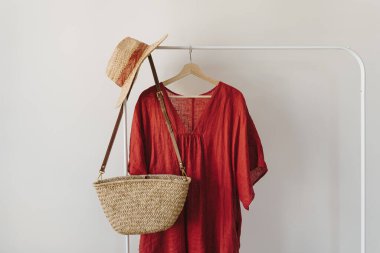 Şık moda kıyafetleri ve aksesuarlar. Kırmızı elbise, hasır şapka, askıda kurumuş ortanca çiçekli saman el çantası. Moda günlüğü, kopyalama alanı olan sosyal medya şablonu