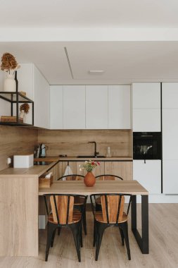 Modern İskandinav ev iç tasarımı. Parlak açık oturma odası, yemek masası, mutfak mobilyası, sandalyeler, dekorasyonlar. Kira konsepti için şık bir daire.