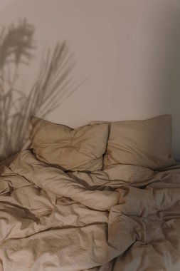 Estetik minimalist yatak odasının içi. Buruşmuş bej bej çarşaflar ve ılık, yumuşak güneş ışığı gölgeleri.