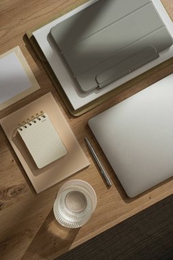 Laptop, tablet, defter ve bir bardak suyla ev ofisinin çalışma alanı düzdü. Sabah işi, iş konsepti. Masada güneş ışığı gölgeleri var. Üst görünüm