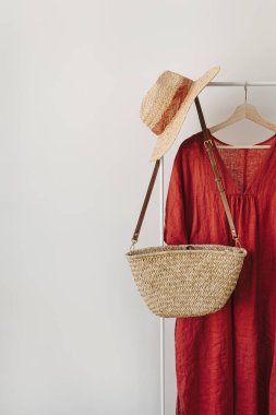 Hasır şapka, saman çanta, kırmızı elbise beyaz duvarın üzerinde askılık.