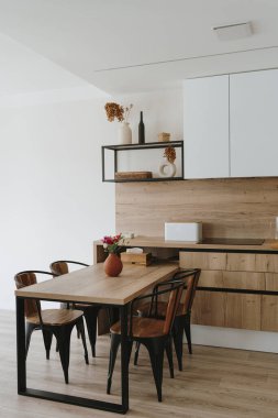 Modern İskandinav ev iç tasarımı. Parlak açık oturma odası, yemek masası, mutfak mobilyası, sandalyeler, dekorasyonlar. Kira konsepti için şık bir daire.