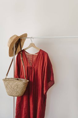 Hasır şapka, saman çanta, beyaz duvarın üzerinde elbise askılığında kırmızı elbise. Moda giysileri, online alışveriş konsepti.