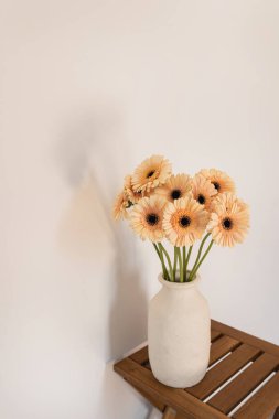 Pastel portakallı gerbera çiçeği buketi ahşap masadaki beyaz kil çömlek içinde. En küçük iç tasarım dekorasyonu