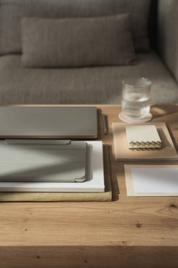 Laptop bilgisayarlı ofis masası çalışma alanı, spiral çevirmeli defter, tablet, masa üzerinde güneş ışığı gölgeli bir bardak su. Günlük, web sitesi, sosyal medya hesabı markalaşması