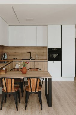 Modern yeni apartman iç tasarımı. Mutfak eşyaları, raflar, yemek masası, sandalyeler olan beyaz mobilyalar. Kiralık daireler