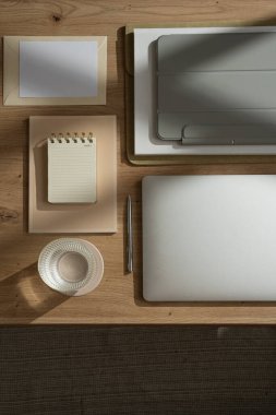 Laptop, tablet, defter ve bir bardak suyla ev ofisinin çalışma alanı düzdü. Sabah işi, iş konsepti. Masada güneş ışığı gölgeleri var. Üst görünüm
