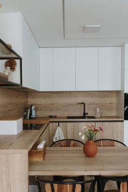 Modern İskandinav ev iç tasarımı. Parlak açık oturma odası, yemek masası, mutfak mobilyası, sandalyeler, dekorasyonlar. Kira konsepti için şık bir daire.