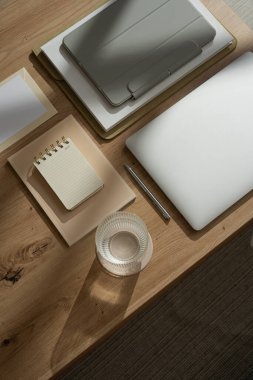 Düz ofis çalışma alanı dizüstü bilgisayarı, bir bardak su, tablet, güneş ışığı gölgesinde kırtasiye malzemesi. Üst düzey estetik lüks bohem kadın patron iş hayatı konsepti