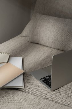 Dizüstü bilgisayar ve ofis belgeleri rahat kanepede, güneş ışığı gölgeli.