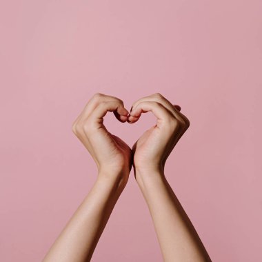 Sevgililer Günü kompozisyonu. Kalp, pembe arka plandaki kadın ellerinden oluşan aşk sembolü. Zarif Sevgililer Günü kartı şablonu