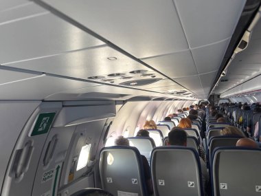 Arkadan gelen insanlarla dolu bir uçakta yolcu koltuğu, cep telefonu fotoğrafı.