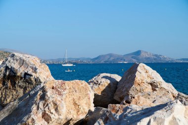 Sakin, masmavi bir deniz ve kayaların arkasında bir yat.