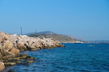 Sakin, masmavi bir deniz kayalık bir kıyısı ve yatı var.