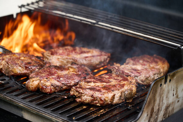 Стейки Черного Ангуса жарят на гриле. Пламя проникает в решетку гриля и жарит мясные стейки