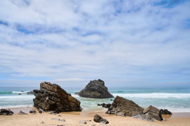 Okyanus dalgaları geniş bir sahilde kayalık kayaların üzerinde süzülür. Praia da Ursa. Portekiz, 2024. Yüksek kalite fotoğraf