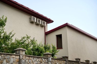 Üç havalandırma ünitesi, taş bir çitin yanındaki barakanın altındaki bir evin duvarına bağlı.