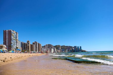 Yüksek modern binaları olan sahil kenti kumlu bir sahil. Açık gökyüzü ve yumuşak dalgalar, güneşin tadını çıkaranlar için ferahlatıcı bir atmosfer yaratır. Benidorm, Alicante, İspanya 10.01.2023