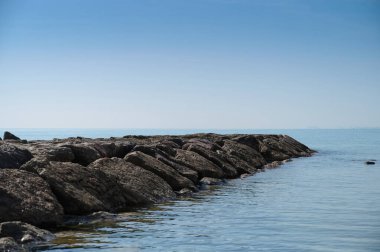 Sağlam bir kayalık, berrak bir gökyüzü ile çevrili sakin mavi sulara doğru uzanıyor. Sahnenin sakinliği huzurlu bir kıyı ortamını yansıtıyor. Rahatlamak için ideal..