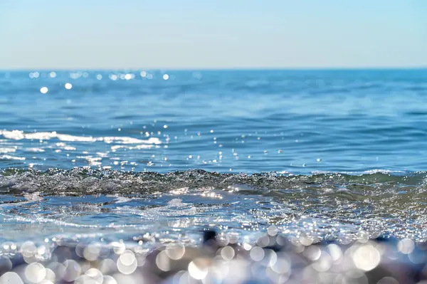 Yumuşak dalgalar kumlu bir plaja yuvarlanıyor, gün ışığında parlıyor. Sakin okyanus ufka doğru uzanıyor, rahatlama ve sükuneti davet ediyor..