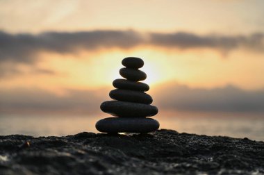 Güneş ufukta batarken beş pürüzsüz taş ustalıkla kayalık gerektiren bir kıyıya istiflenmiştir. Nazik dalgalar ve sıcak renkler, doğayla bir bağ ve sakinlik hissi uyandırır..