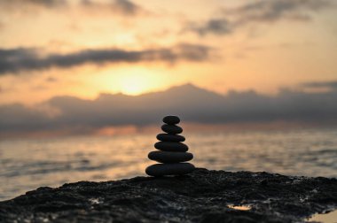 Sakin dalgalar ve yumuşak bulutlar üzerine sıcak renkler düşen güneş batarken engebeli bir sahilde dikkatlice dengelenmiş pürüzsüz taşlardan oluşan bir kule gururla duruyor. Huzur çağrıştırıyor.