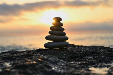 Pürüzsüz taşlardan oluşan dikkatlice dengelenmiş bir kule çarpıcı bir günbatımına karşı görkemli bir şekilde duruyor. Alacakaranlık 'ın canlı renkleri sakin suyu yansıtıyor ve sakin atmosferi güçlendiriyor..